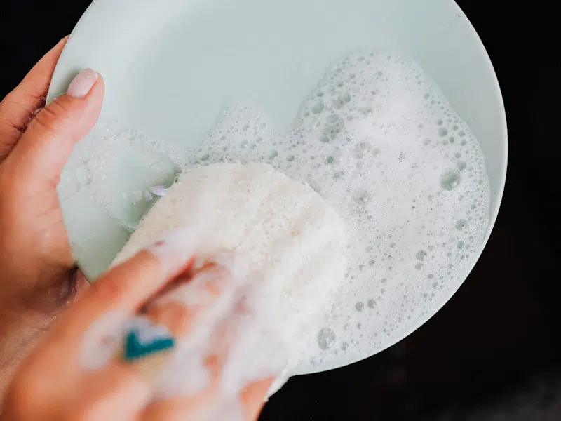 Plate being washed by hand with lots of soapsuds.
