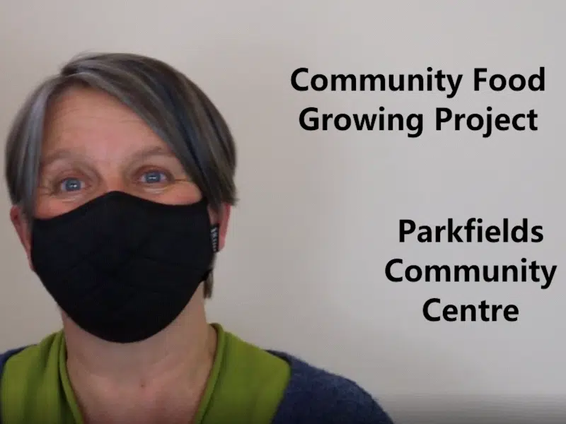 Woman wearing mask in front of sign reading: Community Food Growing Project, Parkfields Community Centre.